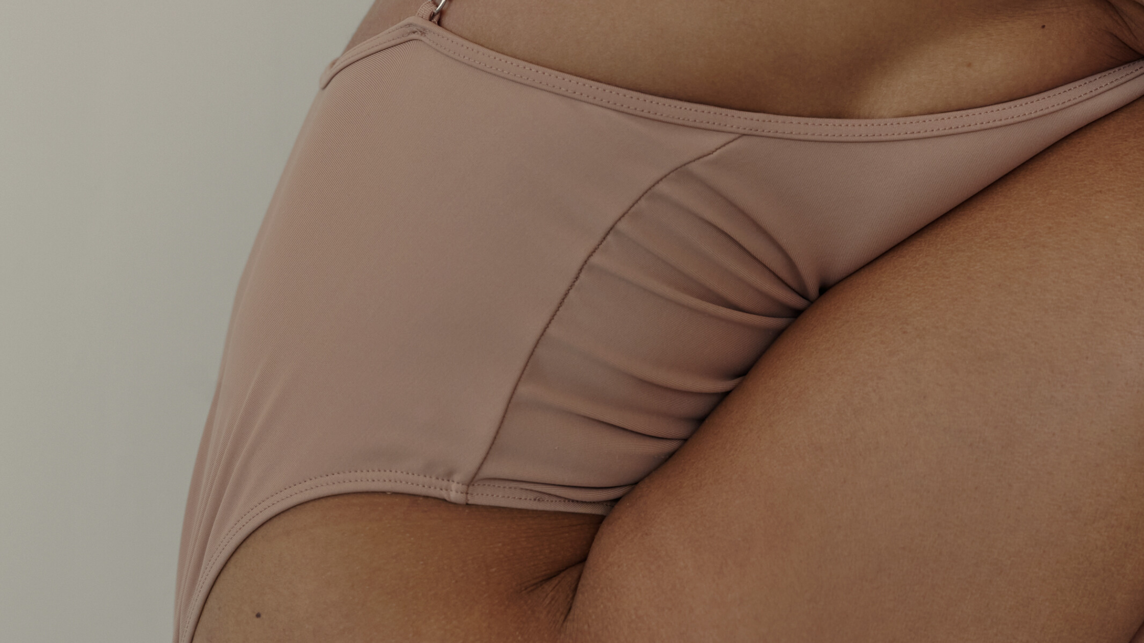 Close-up of a woman’s lower abdomen and hips in nude-colored underwear, symbolizing body awareness and menstrual health.