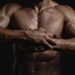 Muscular male torso with crossed arms, symbolising strength, recovery, and the effects of peptide therapy.