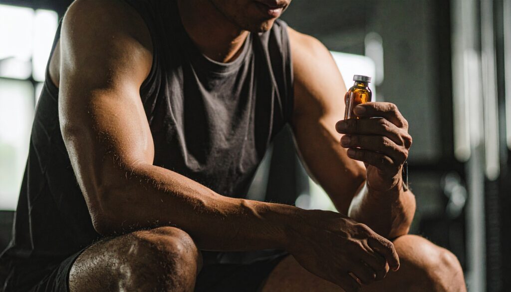 Athletic man holding a small medical vial while seated in a gym, symbolising peptide or SARM use for muscle growth.