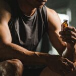 Athletic man holding a small medical vial while seated in a gym, symbolising peptide or SARM use for muscle growth.